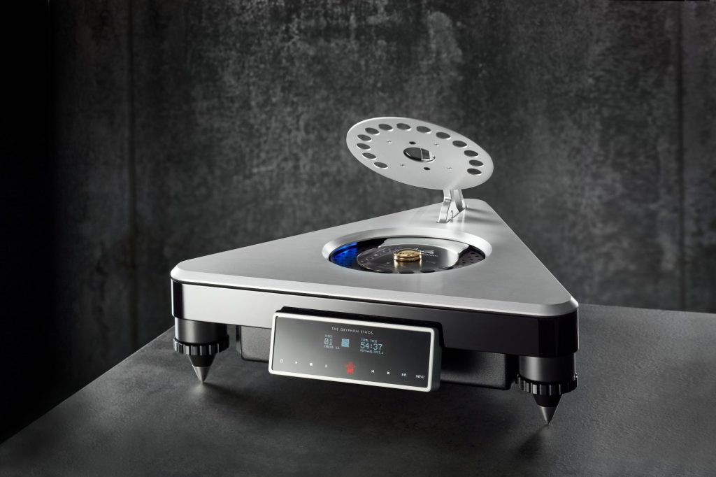 Gryphon Ethos CD player with its top lid raised, showing the illuminated disc platter, against a dark concrete wall