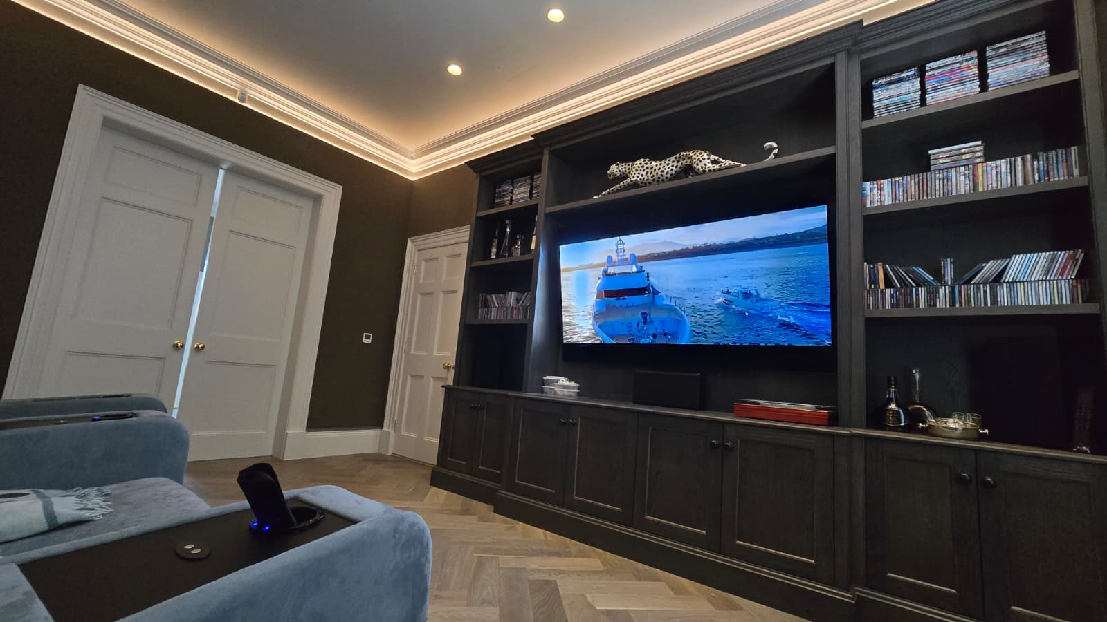 Period country house home cinema with screen in dark-stained bookcase, parquet flooring and cove lighting