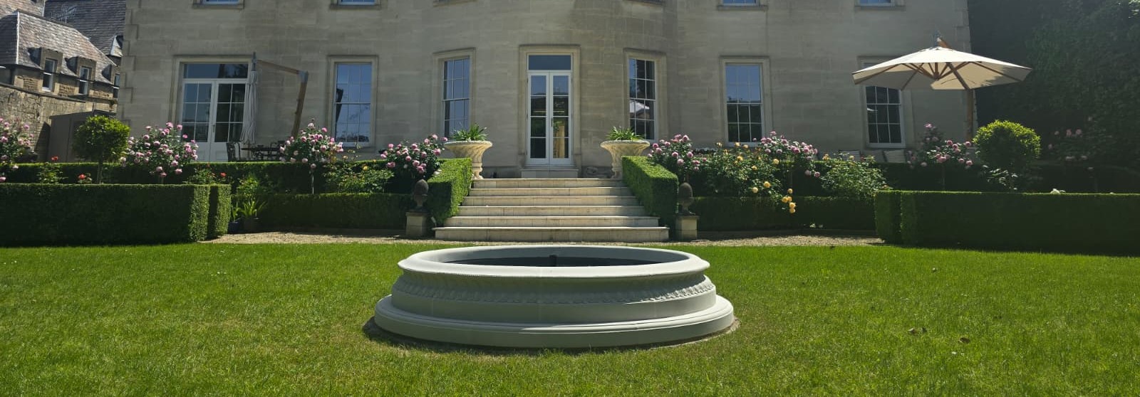 Rear elevation of a period country house with formal parterre garden and stone fountain