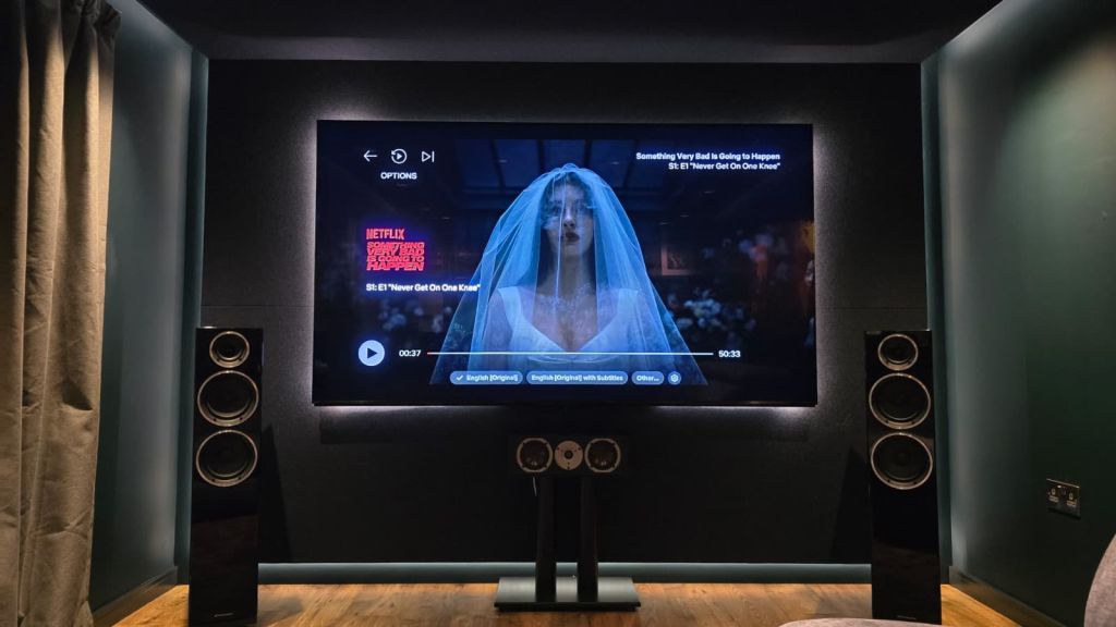 Garden room cinema in Gloucester — screen wall with floating LED front-wall feature, custom acoustic treatment behind petrol-green fabric, designed and built by Hidden Home Technology