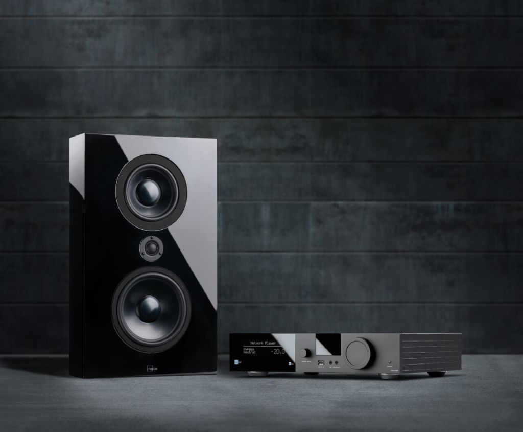 Lyngdorf loudspeaker alongside a Lyngdorf TDAI integrated amplifier in a low-lit lifestyle setting