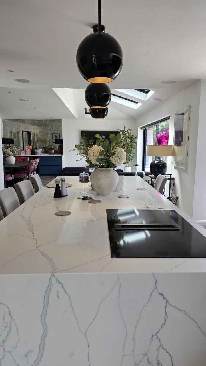 Stone-topped kitchen island beneath pendant lighting with discreet multi-room audio overhead