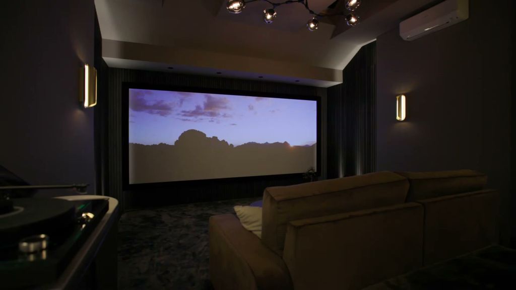 Dedicated home cinema room with a glowing projection screen, fabric-panelled walls and brass wall lights