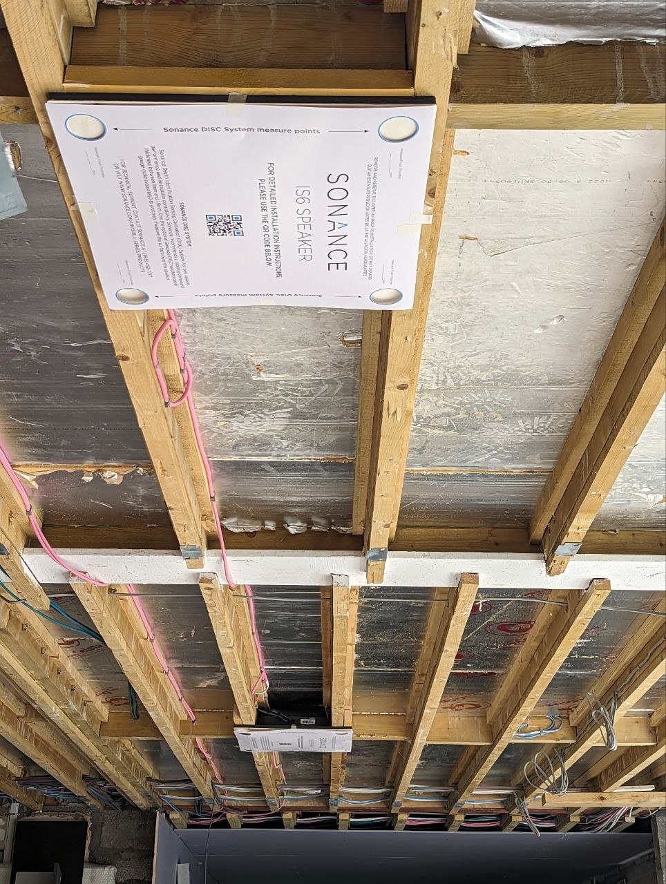 Invisible in-ceiling loudspeaker fixed between ceiling joists before plastering, with its cable run in place