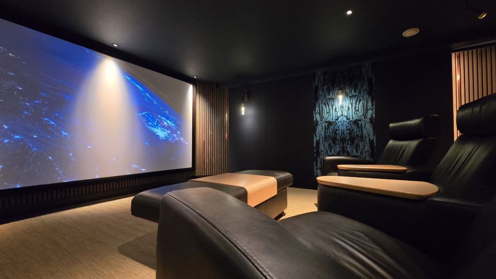 Wide view of the award-winning Steinway Lyngdorf home cinema near Bath with the acoustically transparent screen lit and recliners in the foreground