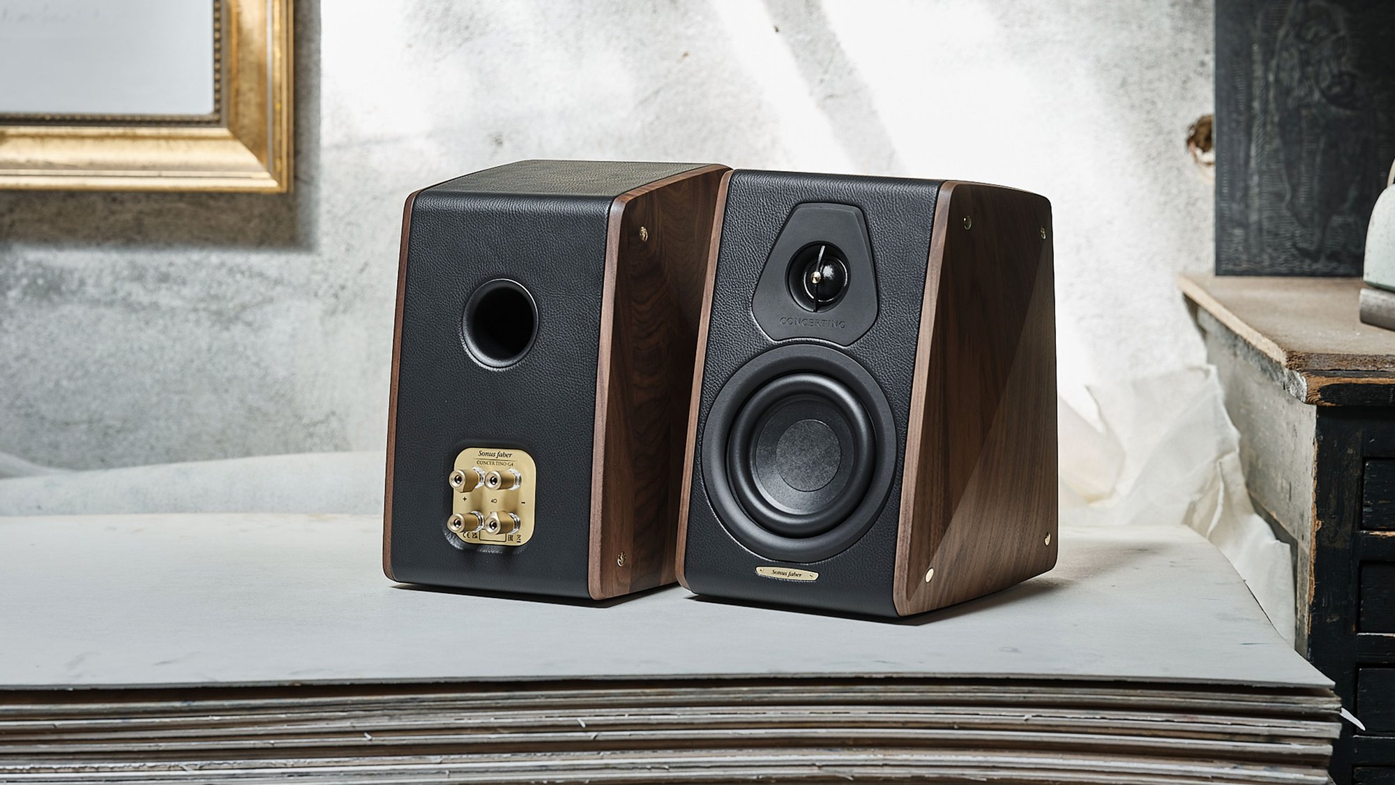 A pair of Sonus Faber Concertino speakers, one with its grille fitted, in a workshop setting