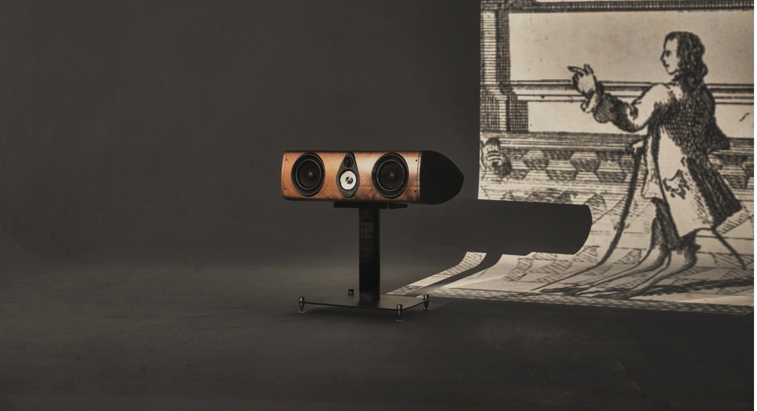 Sonus Faber Olympica Center in walnut on its stand in front of a printed backdrop